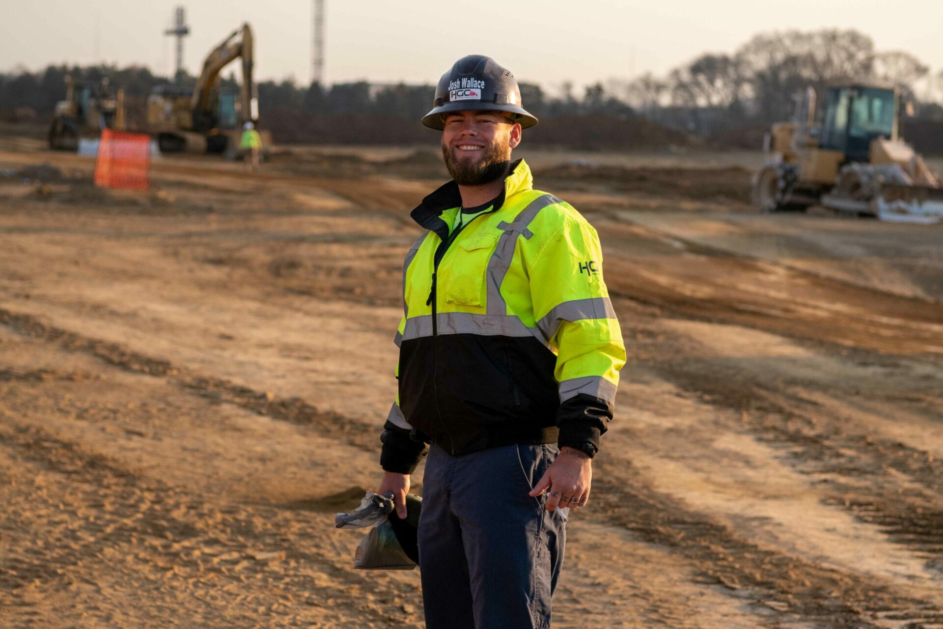 A HGC employee wearing a bright yellow jacket, smiling at the camera while standing in a construction site