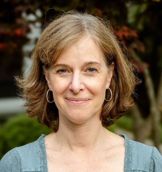 a headshot of a woman wearing a green top and silver hoop earrings