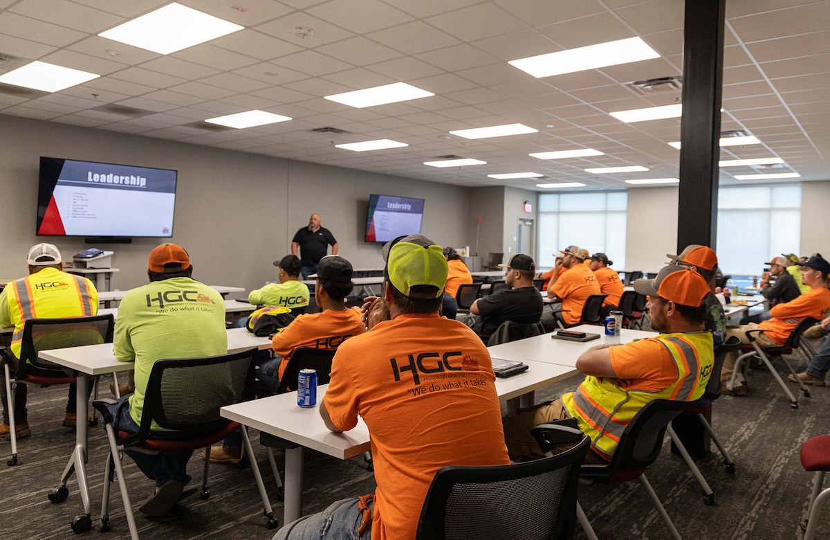 HGC teammates in yellow and orange shirst sitting at tables in a conference room