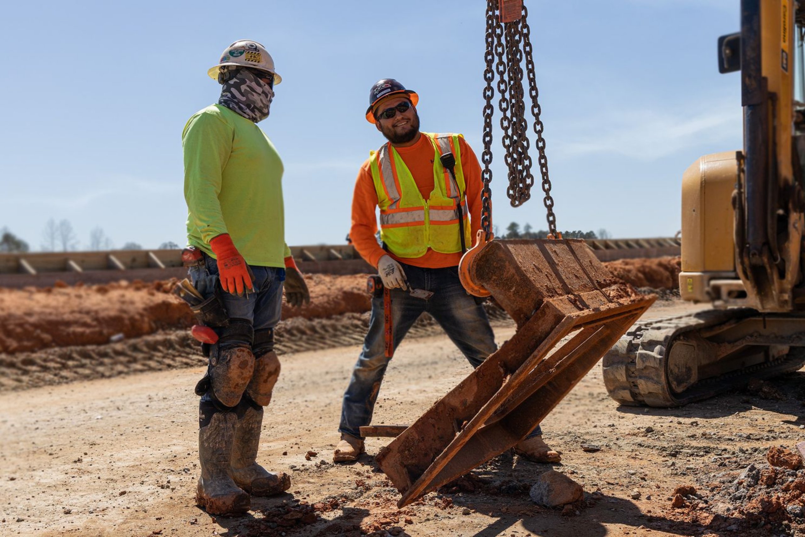 Two construction workers at Hoopaugh Grading Company help move heavy materials around worksite.