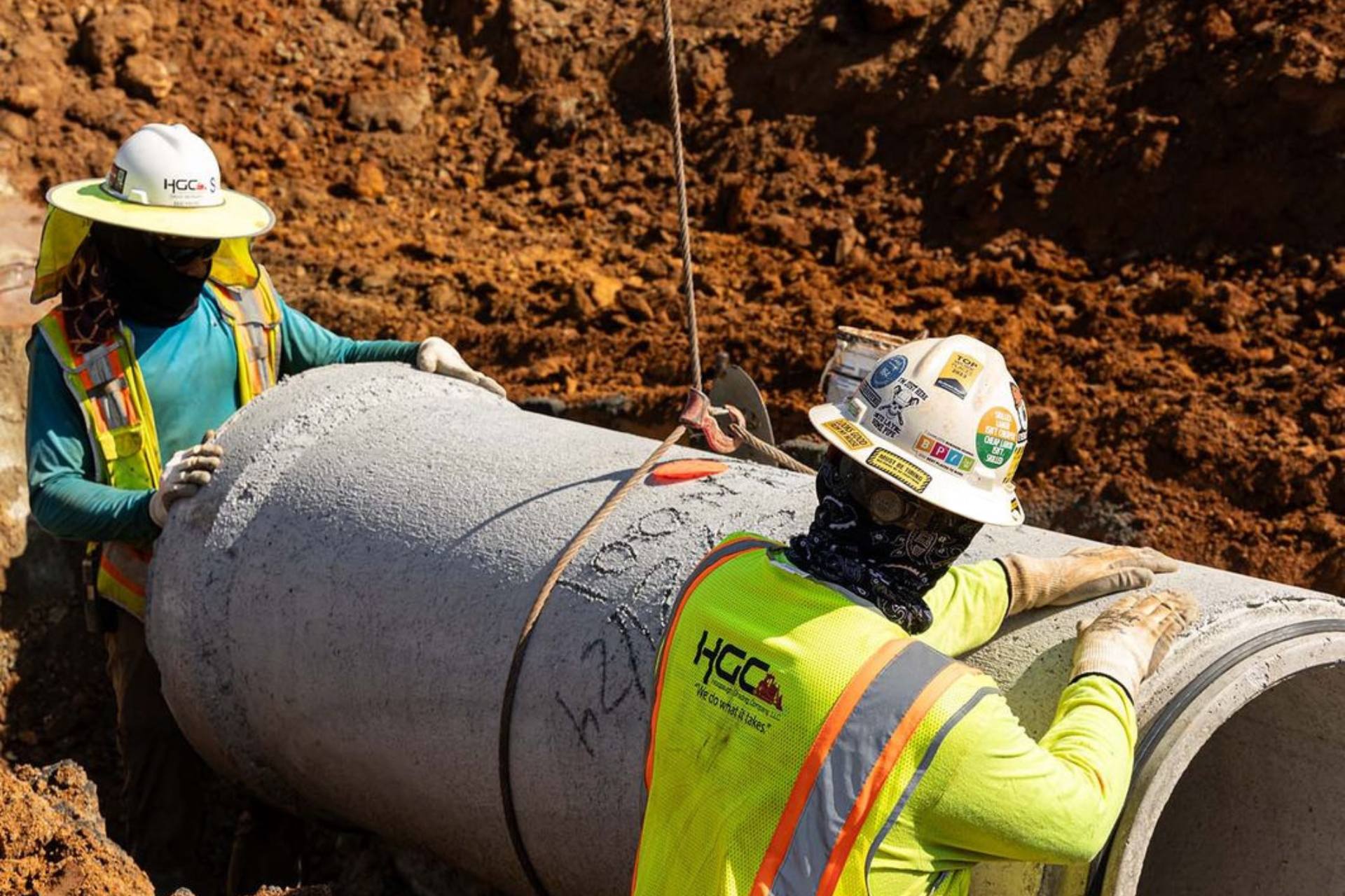 Two Hoopaugh Grading Company teammates help lay concrete pipe on worksite.